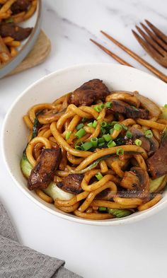 a white bowl filled with noodles and meat on top of a table next to chopsticks