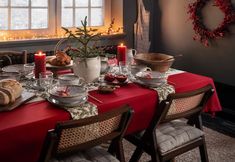 a dining room table set for christmas dinner with candles and dishes on the table in front of it