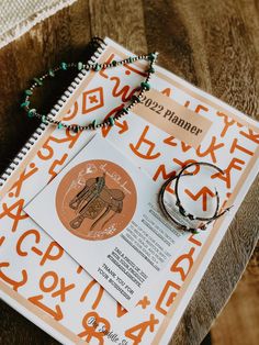 an orange and white book with bracelets on it next to a pair of earrings