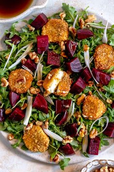 a salad with beets, carrots and nuts on a white plate next to a cup of tea