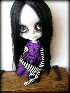 a doll with long black hair wearing a purple dress and striped stockings sitting on top of a wooden table