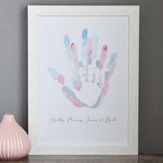 a pink vase sitting on top of a wooden table next to a framed hand print