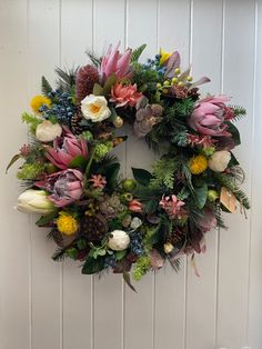 a wreath hanging on the side of a door with flowers and greenery around it