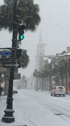 a city street is covered in snow and traffic lights are green as cars drive down the road