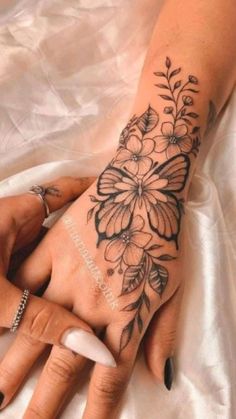 a woman's hand with tattoos on it and flowers on the wrist is shown