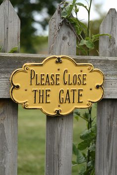 a yellow sign that says please close the gate on a wooden fence with green leaves