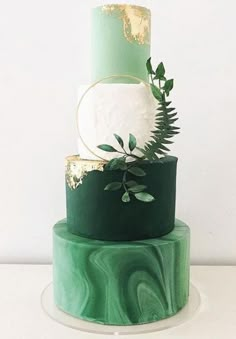 a three tiered green and gold wedding cake with greenery on the top layer