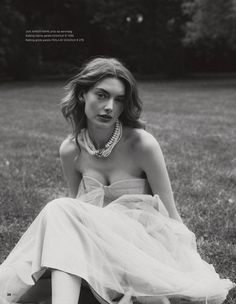 a woman sitting on the ground wearing a dress and necklace in black and white photo