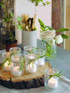 there are many candles on the table with some flowers in vases and greenery