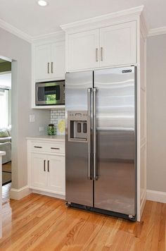 a stainless steel refrigerator in a kitchen with white cabinets and wood floors, along with hardwood flooring