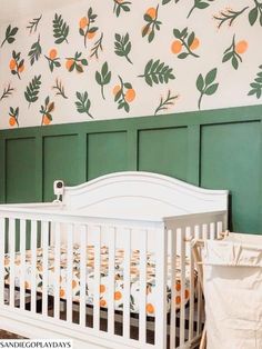 a white crib in front of a green wall with oranges on the wall