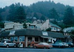 cars are parked in front of a small building on the side of a road with mountains in the background