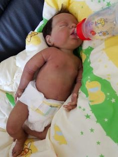 a baby laying on top of a bed with a bottle in it's mouth