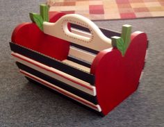 an apple shaped wooden toy with handles on carpeted floor next to rug and wall