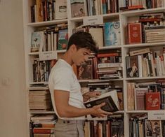 a man reading a book in front of a bookshelf full of books on it