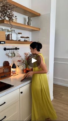 a woman in a yellow dress is standing at the kitchen counter and looking into an oven