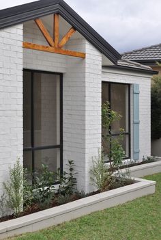 a white brick house with blue shutters on the windows and plants in the front