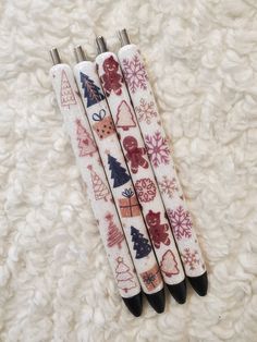 three christmas themed pens sitting on top of a white carpet with snowflakes and trees