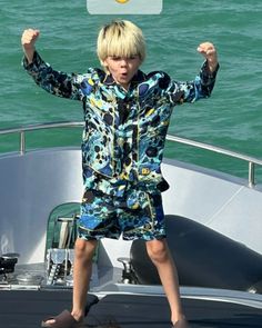 a young boy standing on the back of a boat holding up a sign with his hands