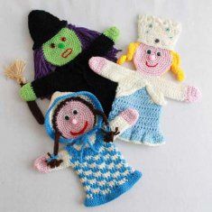 three knitted dolls laying next to each other on a white surface with one wearing a blue dress