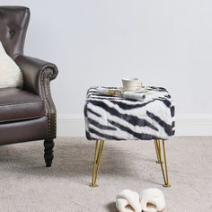 a zebra print blanket on the floor next to a chair and foot stool with slippers