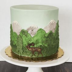 there is a green cake decorated with mountains and a deer on the bottom, along with pine trees