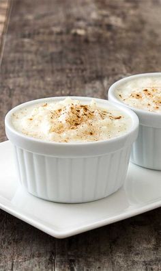 two white dishes filled with food on top of a wooden table