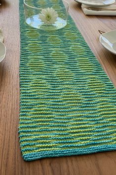 a knitted table runner on a wooden table with plates and bowls in the background