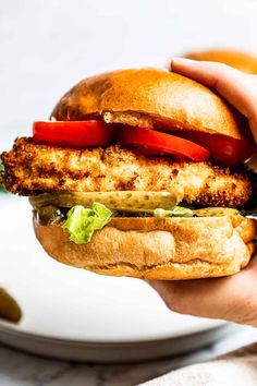 a chicken sandwich with lettuce, tomato and pickles on a white plate