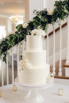 a white wedding cake sitting on top of a table next to candles and greenery