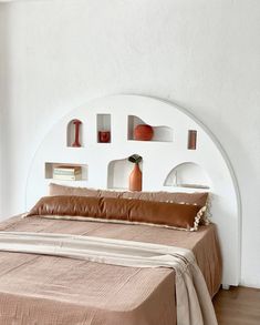 a bed in a room with white walls and wooden flooring, along with shelves on the wall