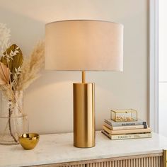 a lamp on a table next to a vase with flowers in it and some books