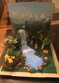 a paper mache landscape with rocks and plants in the foreground is a waterfall