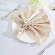 a white plate topped with a napkin and utensils next to a flower arrangement