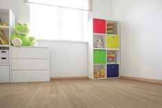 an empty room with white walls and wooden flooring is decorated with brightly colored bookshelves