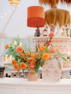 an arrangement of orange flowers in a vase on top of a table with a sign