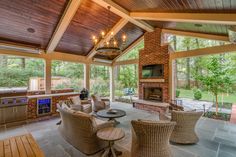 an outdoor kitchen and dining area with wood ceilinging, wicker furniture, and large windows