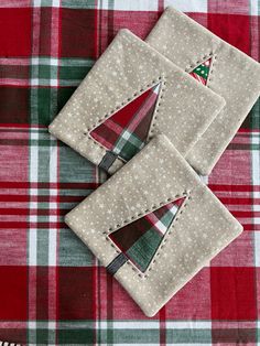 three small christmas trees are placed on top of each other in the middle of a red and green checkered tablecloth