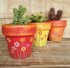 three painted flower pots sitting on top of a wooden table