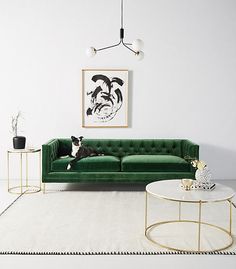 a living room with a green velvet couch and coffee table in front of a painting on the wall