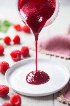 raspberry sauce being drizzled onto a plate with raspberries