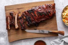 ribs, macaroni and cheese on a cutting board with a knife next to it