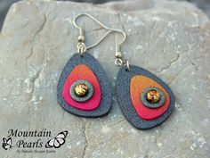 two pairs of earrings with colorful designs on them sitting on top of a stone slab