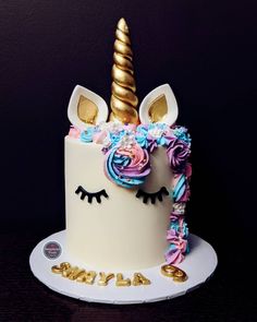 a white cake decorated with pink, blue and gold icing has a unicorn horn on top