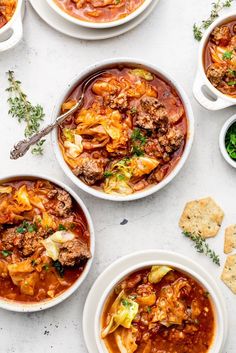 several bowls of soup on a table next to crackers and breads, with one bowl filled with meat