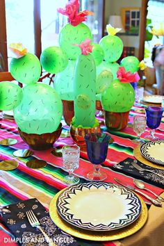 the table is set with plates, cups and utensils in front of a cactus - themed centerpiece