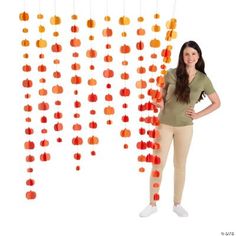 a woman standing in front of a string of orange and red objects hanging from the ceiling