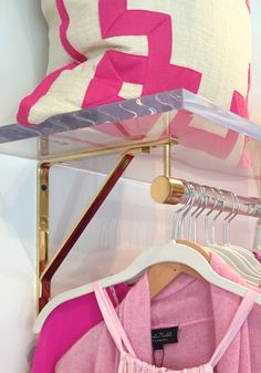 pink and white clothes are hanging on a rack next to a pillow with a gold hanger