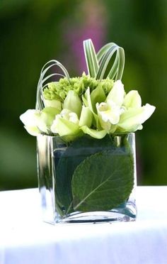 a glass vase filled with flowers and greenery on top of a white table cloth