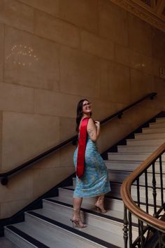 a woman in a blue dress is standing on the stairs with her arms up and smiling